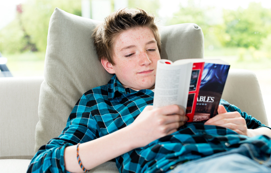 Adolescent allongé sur un canapé en train de lire un livre