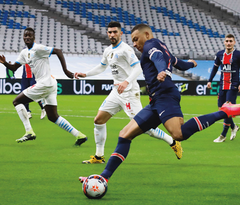 Kylian Mbappé frappe le ballon de football et les adversaires le regardent.